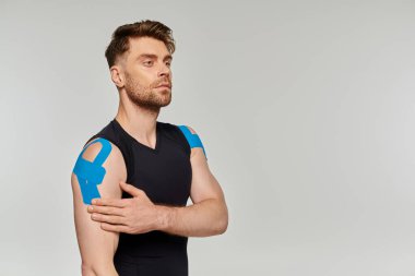 Siyah spor elbiseli yakışıklı adam Kineziyolojik bantlarla poz veriyor ve başka tarafa bakıyor.