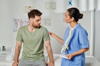 Çekici doktor omurga modelini tutuyor ve randevusu sırasında hastasına danışıyor.
