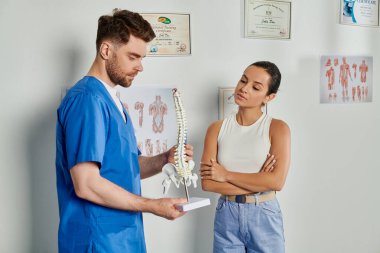 Çekici kadın hasta ellerinde omurga modeliyle yakışıklı sakallı doktora bakıyor.