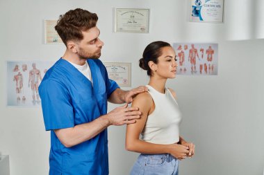 Mavi kostümlü yakışıklı doktor, genç bayan hastasının kaslarını kontrol ediyor.