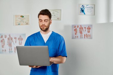 good looking bearded professional doctor in blue medical costume working on his laptop, healthcare clipart
