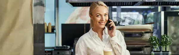 stock image cheerful administrator with coffee to go talking on smartphone and looking at camera in cafe, banner