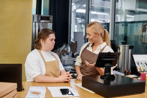 smiling cafe administrator showing cash terminal to young woman with ...