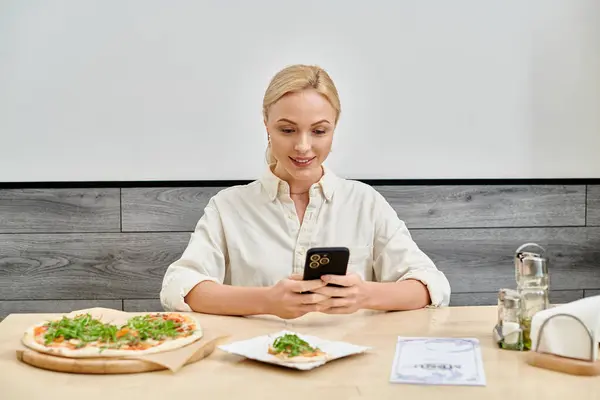 Sorrindo Mulher Loira Mensagens Smartphone Perto Deliciosa Pizza Mesa Moderno — Fotografia de Stock
