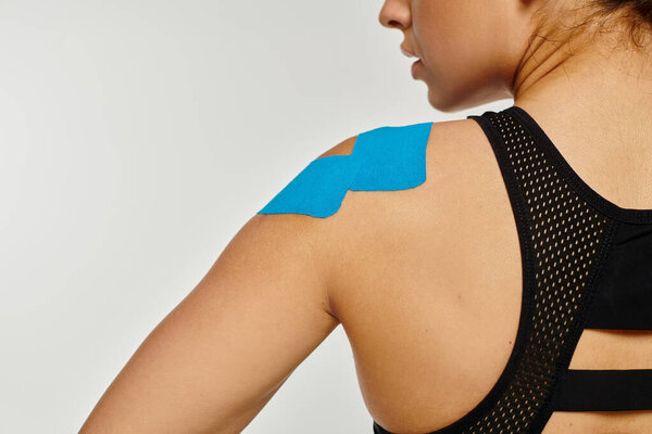 cropped view of young woman in black comfy sport wear with kinesiological tapes on her shoulder