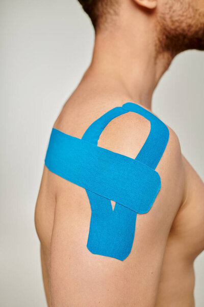cropped view of man with blue kinesiological tapes on his shoulder and back on gray background