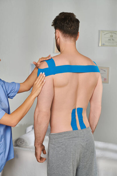 cropped view of young doctor next to her male patient in sweatpants with kinesiological tapes