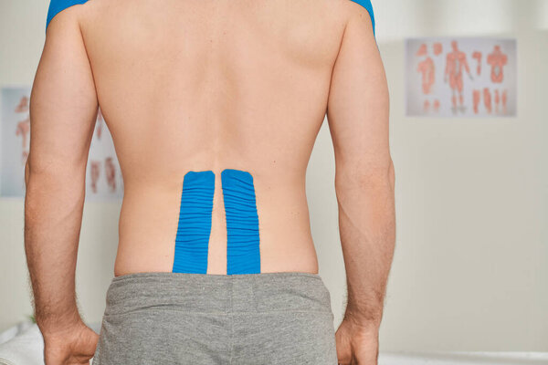 cropped back view of man in gray sweatpants with kinesiological tapes on his back, healthcare