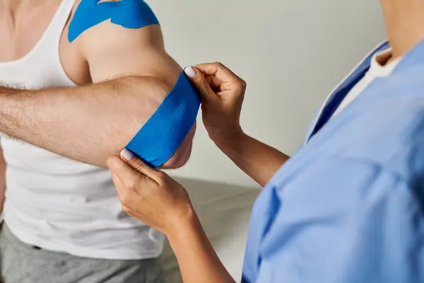 stock image cropped view of female doctor in medical costume putting kinesiological tape on elbow of her patient