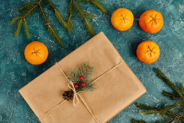 Olgun mandalların yanında süslü hediye kutusu ve mavi desenli arkaplanda çam dalları, Noel teması