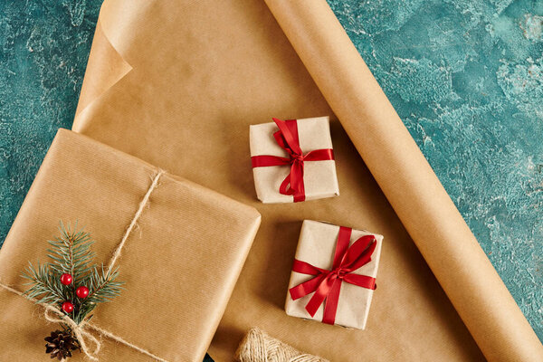 gift boxes with ribbons and pine branch with holly berries on craft paper and blue textured surface
