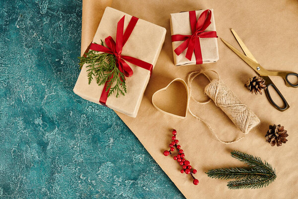 gift boxes and pine decor with holly berries near scissors and craft paper on blue backdrop