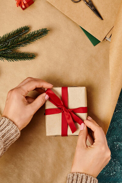 cropped view of woman decorating box with red ribbon on craft paper, handmade gift, vertical banner