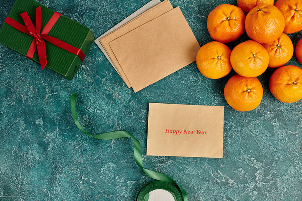 envelope with happy new year near greeting near mandarins and gift box with ribbon on blue backdrop