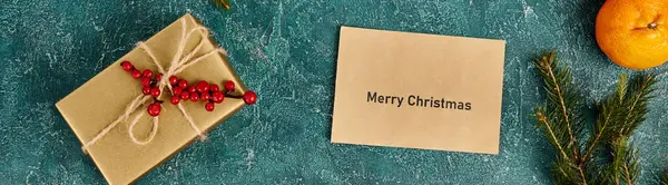 Mandarin 'in yanında mutlu noel zarfları ve mavi dokuda kutsal böğürtlenler olan hediye kutusu, afiş