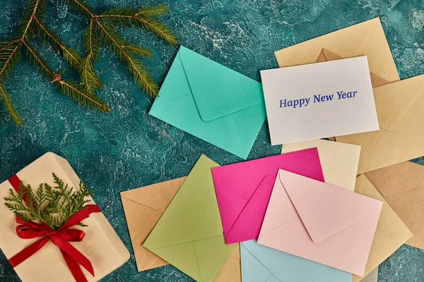 stock image colorful envelopes and gift box near  pine branches on blue rustic surface, happy new year lettering