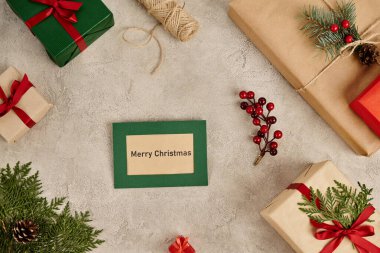 Hediye kutularının yanında mutlu Noeller ve gri desenli yüzey üzerinde şenlikli Noel süsleri.