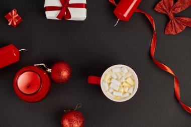 Kırmızı, parlak Noel dekorunun yanında lokum ve siyah arka planda takılar olan bir fincan sıcak çikolata.