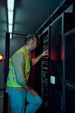 handsome technician with beard in safety vest inspecting data center attentively, maintenance clipart