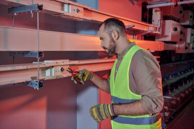 good looking pensive technician in safety vest and gloves working with pliers in data center clipart