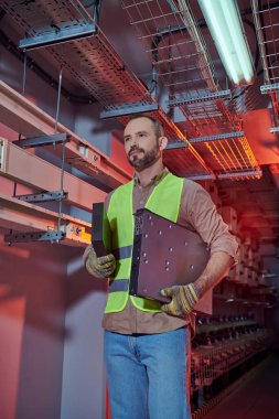 handsome concentrated man in safety vest and gloves working hard and looking away, data center clipart