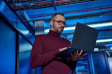 concentrated handsome specialist with beard and glasses in turtleneck working hard on his laptop clipart