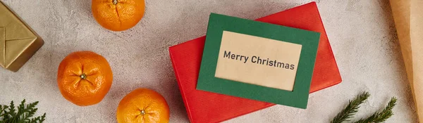 stock image tangerines and Merry Christmas greeting card near presents on textured surface, horizontal banner