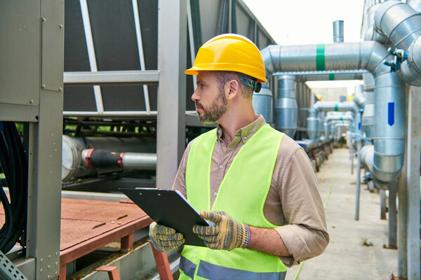 симпатичный сфокусированный техник в защитном шлеме держит буфер обмена и смотрит в сторону, дата-центр