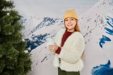 cheerful little girl standing near fir tree with mountain backdrop smiling at camera, fashion clipart