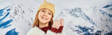 preadolescent cute girl with snow in hands smiling cheerfully at camera, fashion and style, banner clipart