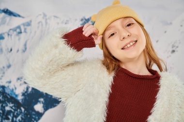 Şapkalı neşeli genç bir kızın portresi. Elleri başının yanında. Kameraya, modaya neşeyle gülümsüyor.