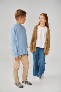 Mavi kazaklı çocuğa gülümseyen örülü hırkalı neşeli küçük kız, moda konsepti.