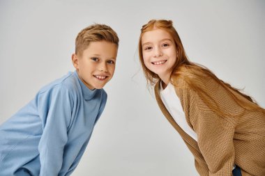 Moda konsepti olan, kameraya neşeyle gülümseyen, modaya uygun giyinmiş iki küçük çocuk.