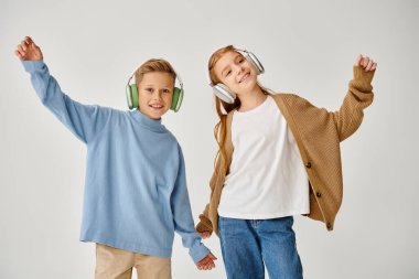 cheerful little children in casual clothes with headsets posing in motion and smiling at camera clipart