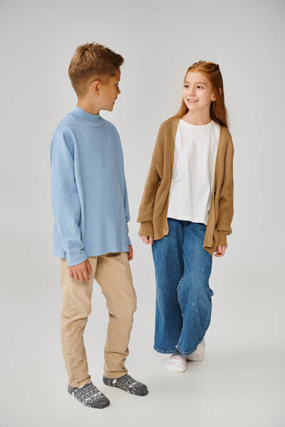 joyous little girl in knitted cardigan smiling at preteen boy in blue sweatshirt, fashion concept