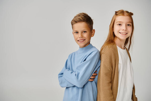 cheerful preteen children in casual warm attires posing back to back looking at camera, fashion