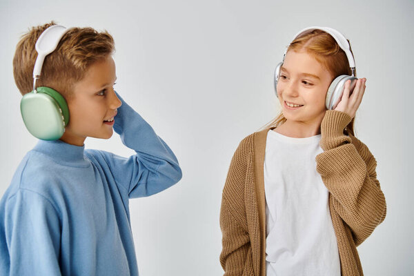 cheerful little children in warm trendy clothes with headphones smiling at each other, fashion