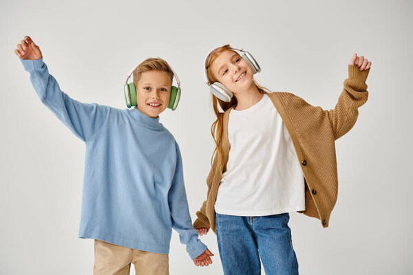cheerful little children in casual clothes with headsets posing in motion and smiling at camera