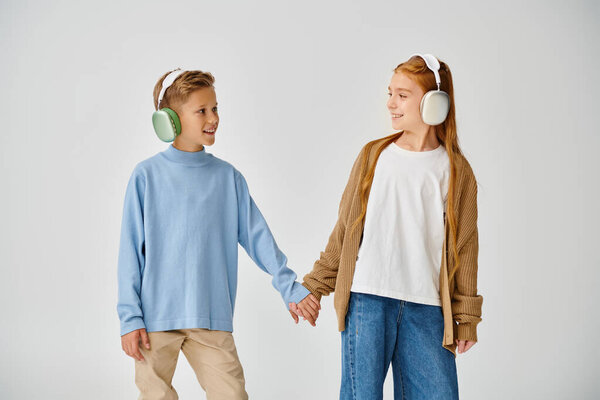 preteen friends in casual attires with headsets holding hands and smiling at each other, fashion