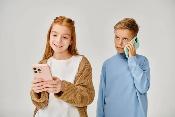 stock image focused little boy talking by phone near his cheerful friend looking at her mobile, fashion concept