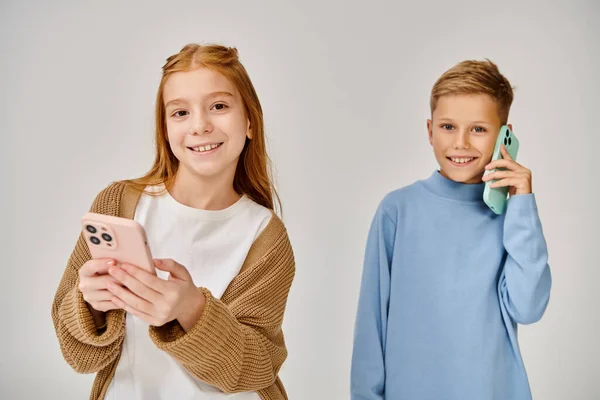 joyous little boy talking by phone next to his jolly peer smiling at camera, fashion concept