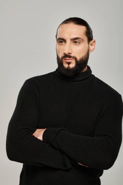 Sakallı yakışıklı Arap adamın portresi gri arka planda çapraz kollarla poz veriyor.