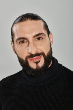 portrait of happy good looking arabic man with beard posing in turtleneck on grey backdrop clipart