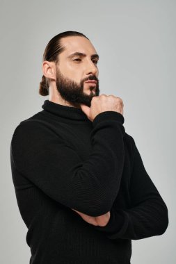portrait of pensive arabic man in turtleneck touching beard while thinking on grey backdrop clipart