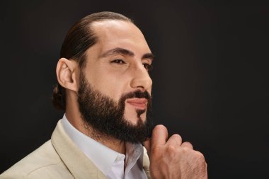 Beyaz gömlekli ve ceketli yakışıklı sakallı Arap adam siyah arka plana bakıyor.