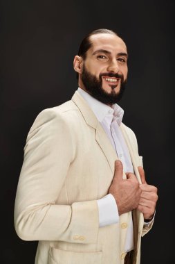 Beyaz gömlekli, siyah arka planda poz veren neşeli ve sakallı Arap bir adam.