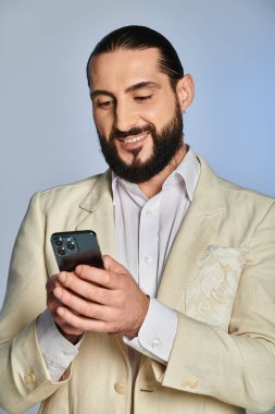 Beyaz sakallı mutlu adam gri arka planda akıllı telefon kullanıyor, şık giyiniyor.