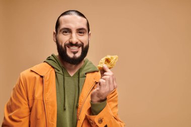 Ballı baklava tutan mutlu bir adam bej renkli, geleneksel ortadoğu tatlısına bakıyor.
