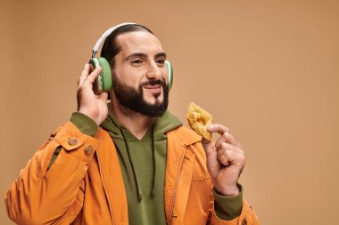 cheerful man in headphones holding honey baklava on beige background, middle eastern dessert clipart