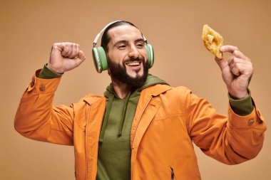 Kulaklıklı mutlu bir Arap adam bej arka planda bal baklavası tutuyor, Orta Doğu tatlısı